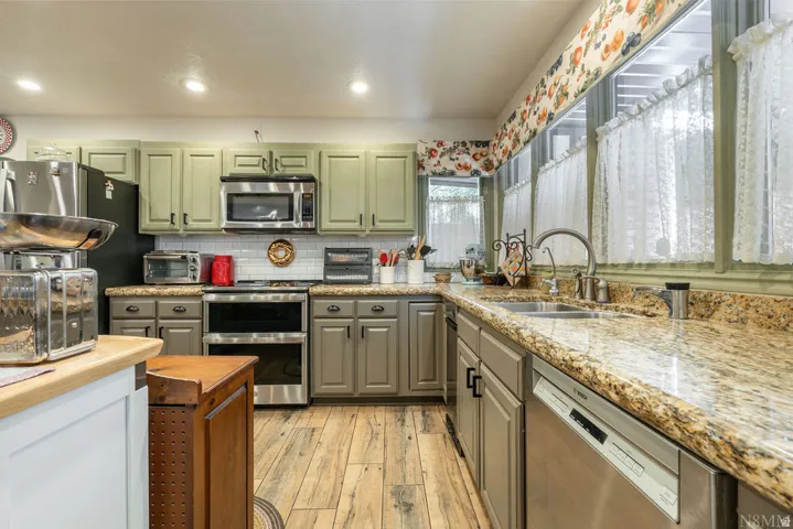 Kitchen featuring light green cabinetry, wood-finish flooring, and granite countertops