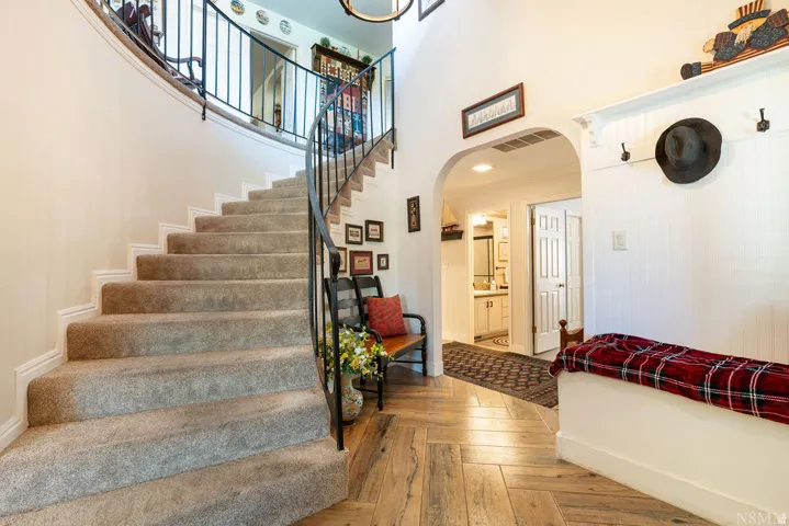 Entryway featuring a curved staircase with carpeted treads and wrought iron railing, vaulted ceilings, wood-finish flooring in a herringbone pattern, and an arched doorway leading to an additional space