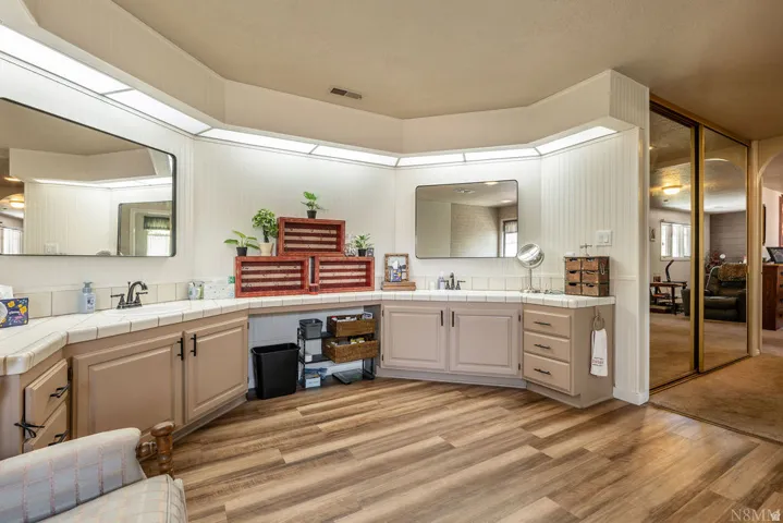Expansive vanity area featuring dual sinks, broad mirrors, recessed lighting, and wood-finish flooring