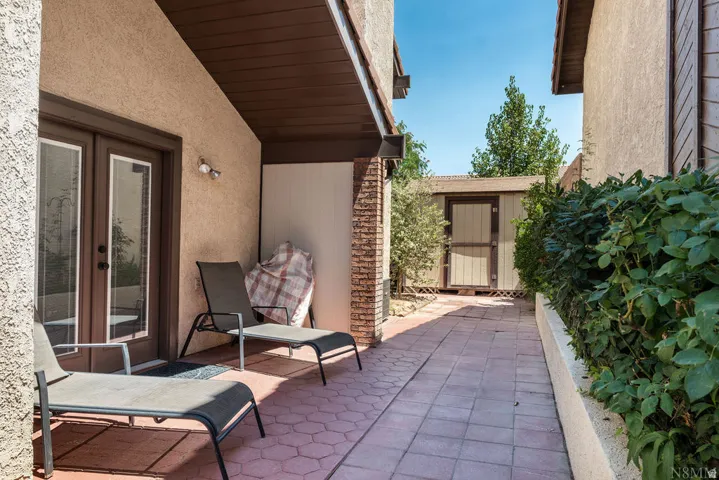 Private patio with textured stucco exterior, brown trim, and dual glass-paneled French doors and storage shed
