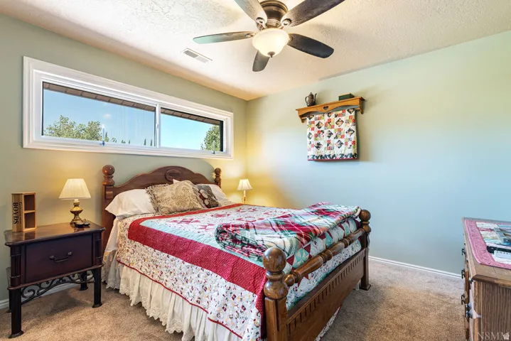 Carpeted bedroom featuring a ceiling fan with integrated lighting, a wide window, and light green wall paint