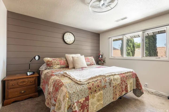 Bedroom featuring a shiplap accent wall, three pane windows, ceiling fan, and carpeted flooring