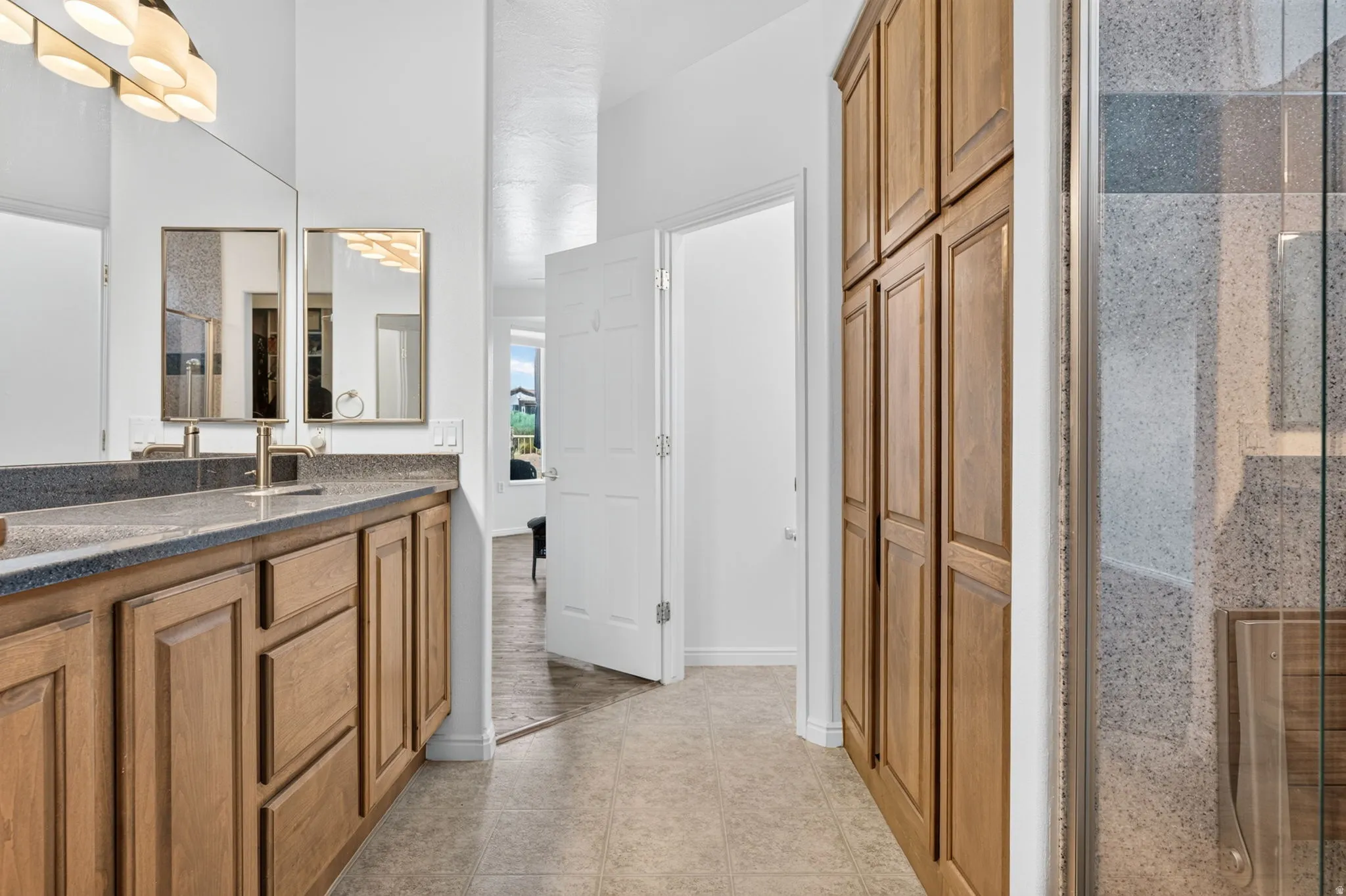 Bathroom vanity with dual sinks and wood-finish cabinetry, complemented by a floor-to-ceiling storage cabinet