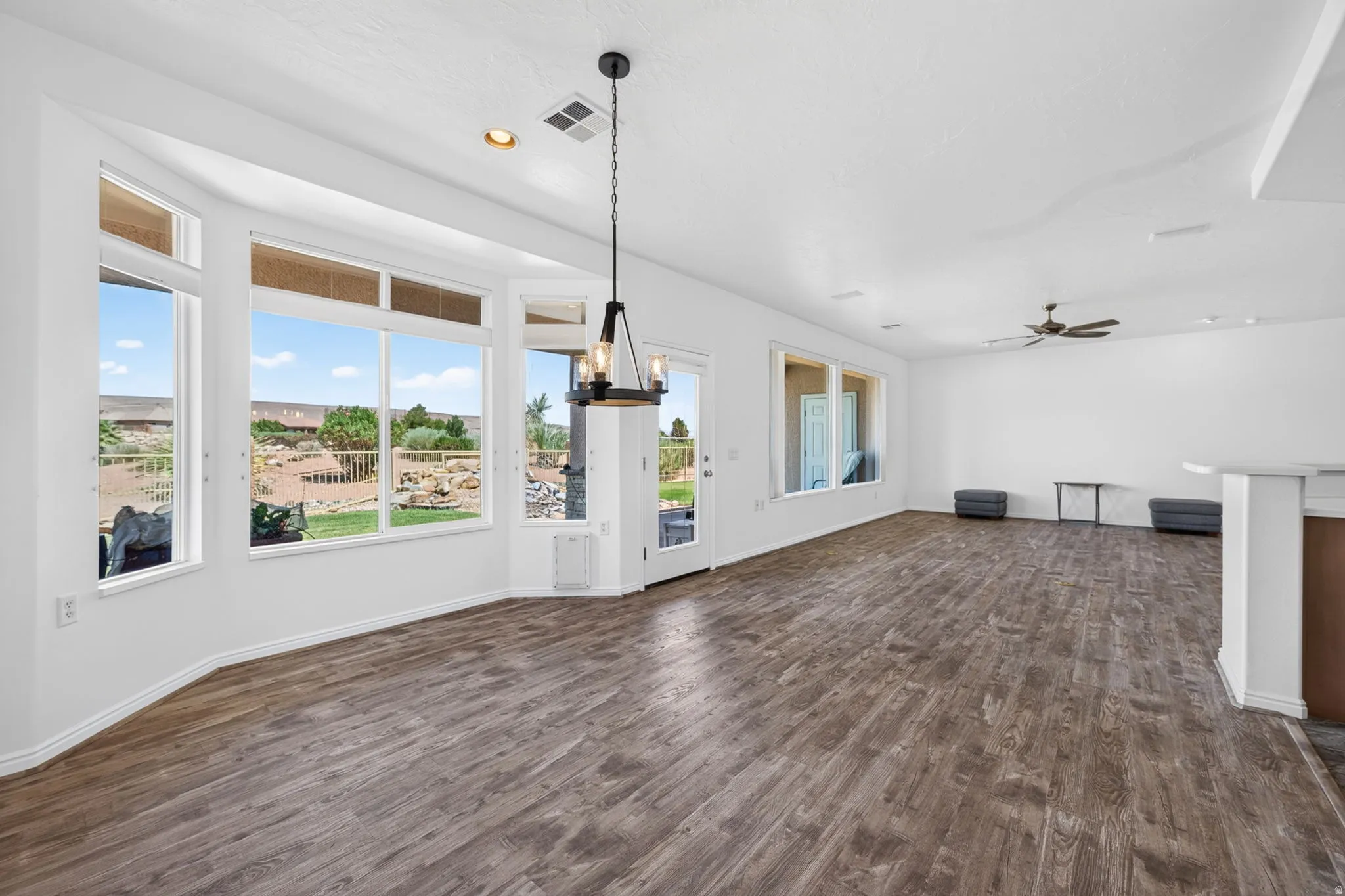 Spacious living area featuring expansive bay windows, wood-finish flooring, and a contemporary chandelier