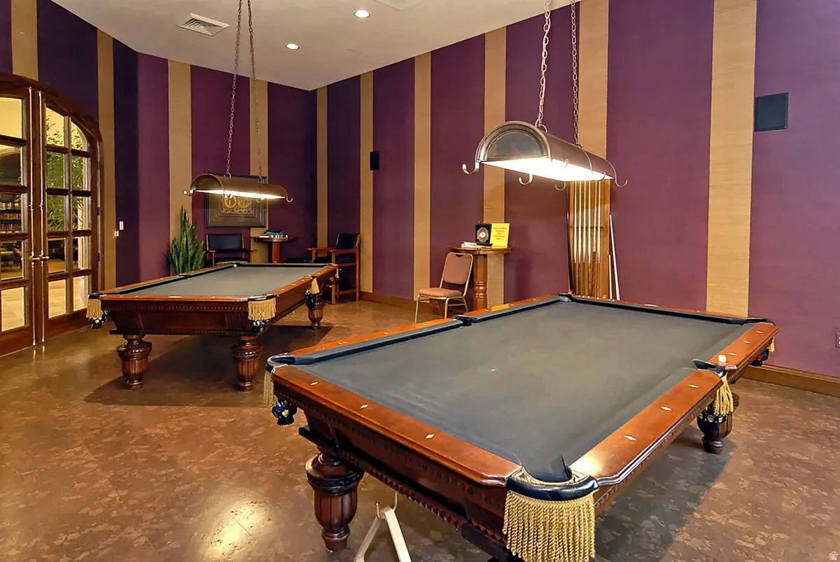 Elegant recreation room featuring two professional-grade pool tables with wood-finish frames and slate playing surfaces, complemented by pendant lighting with brass accents