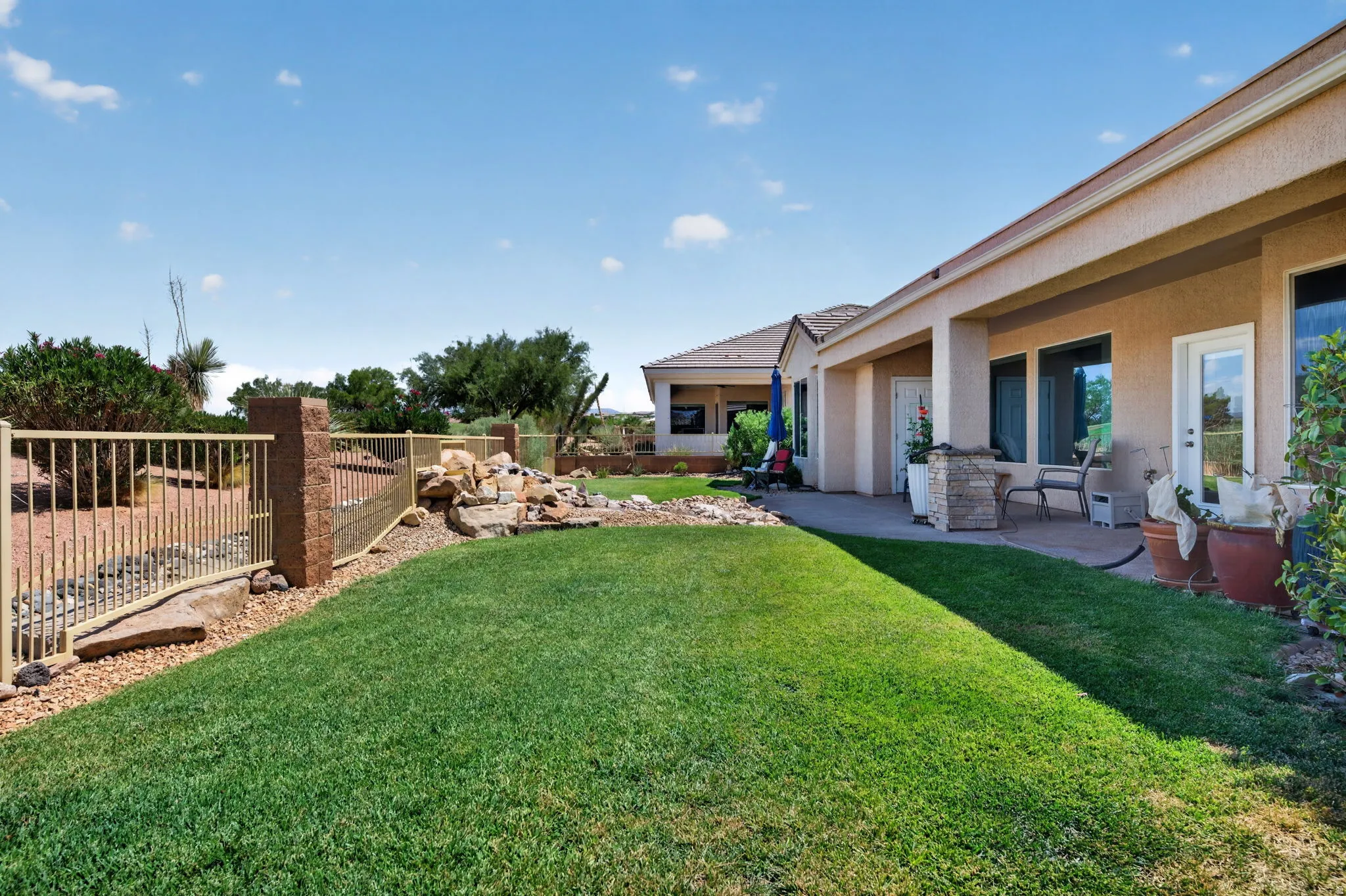 Expansive backyard featuring a lush lawn, a rock garden with a water feature, and a stone patio area