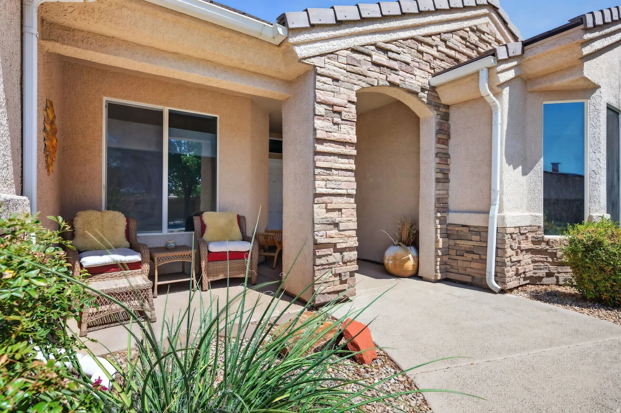 Stucco exterior featuring stacked stone accents, covered entry, front patio, and low-maintenance landscaping