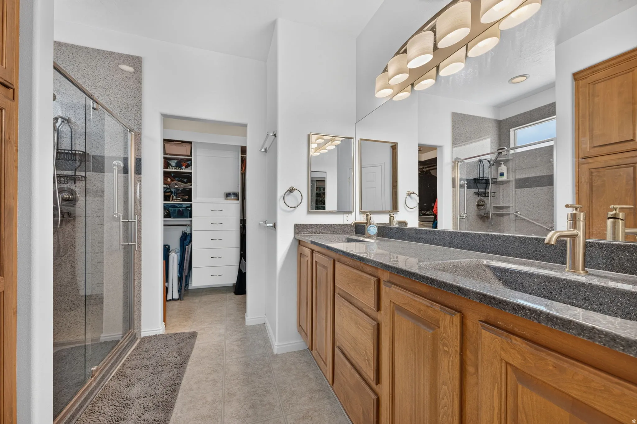 Dual vanity with dark stone countertop, integrated sinks, and brass-tone fixtures
