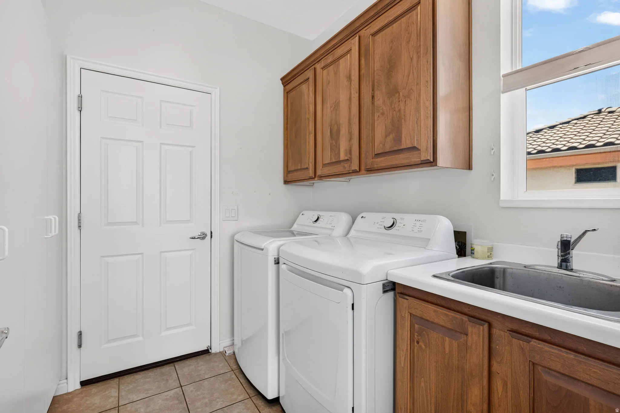 Dedicated laundry area featuring a utility sink, wood-finish cabinetry, and tiled flooring