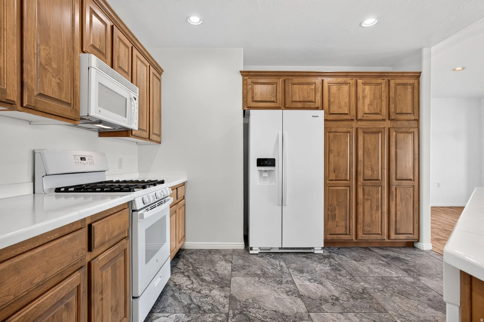 Kitchen featuring extensive wood cabinetry, solid surface countertops, white appliances, recessed lighting, and patterned tile flooring