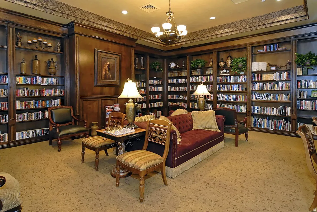 Sophisticated home library featuring floor-to-ceiling built-in cabinetry with glass-front display cases, extensive shelving throughout, decorative crown molding, recessed ceiling lighting, and a rich wood-finish interior