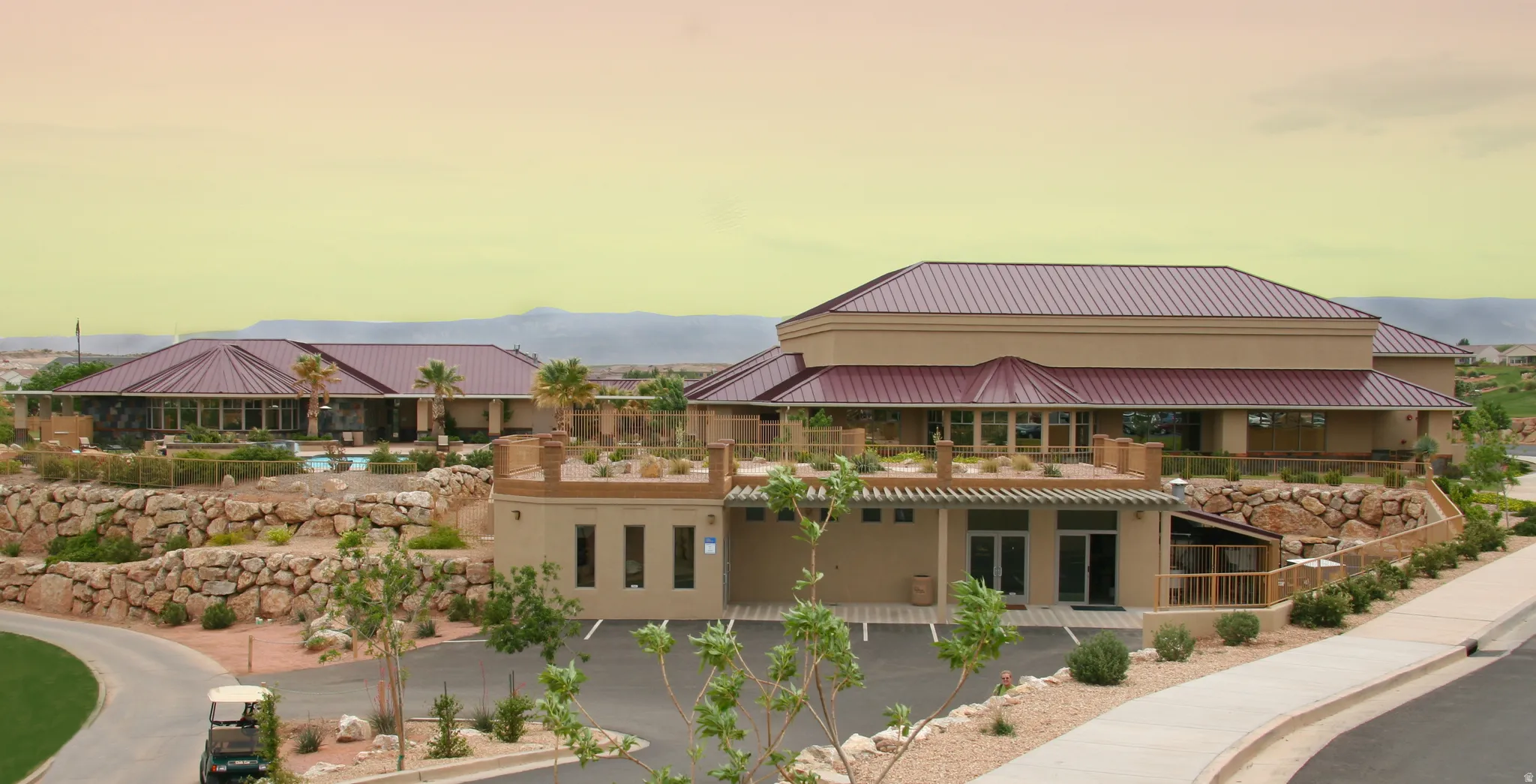 Expansive property featuring multiple structures with complementary architectural styles, a large parking area, and desert-style landscaping