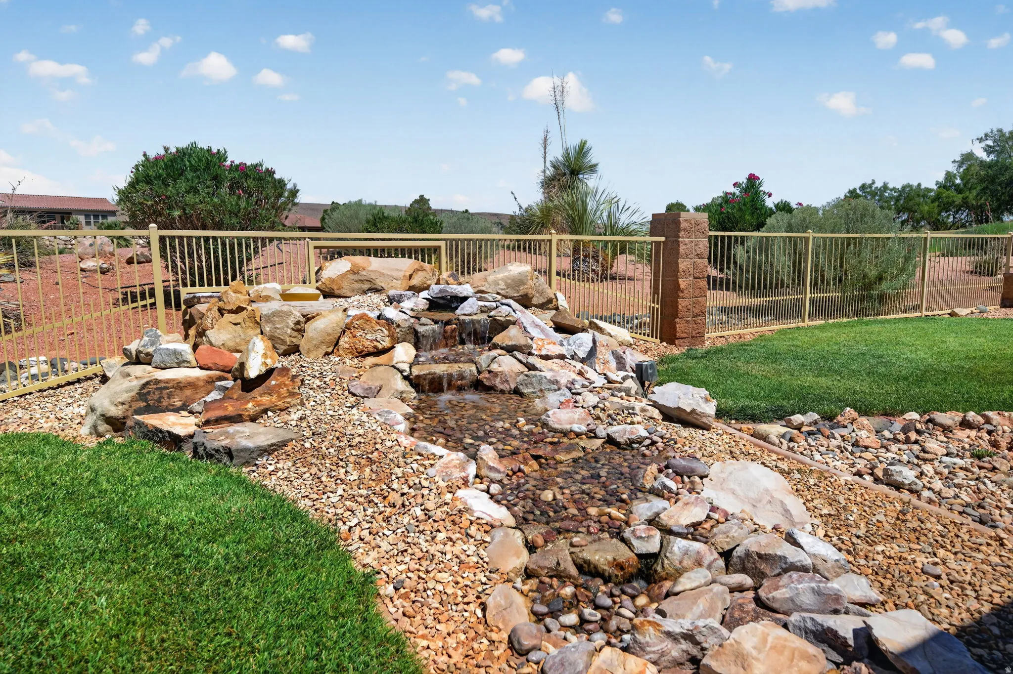 Outdoor water feature with natural rockery and flowing water, bordered by a manicured lawn and decorative gravel landscaping