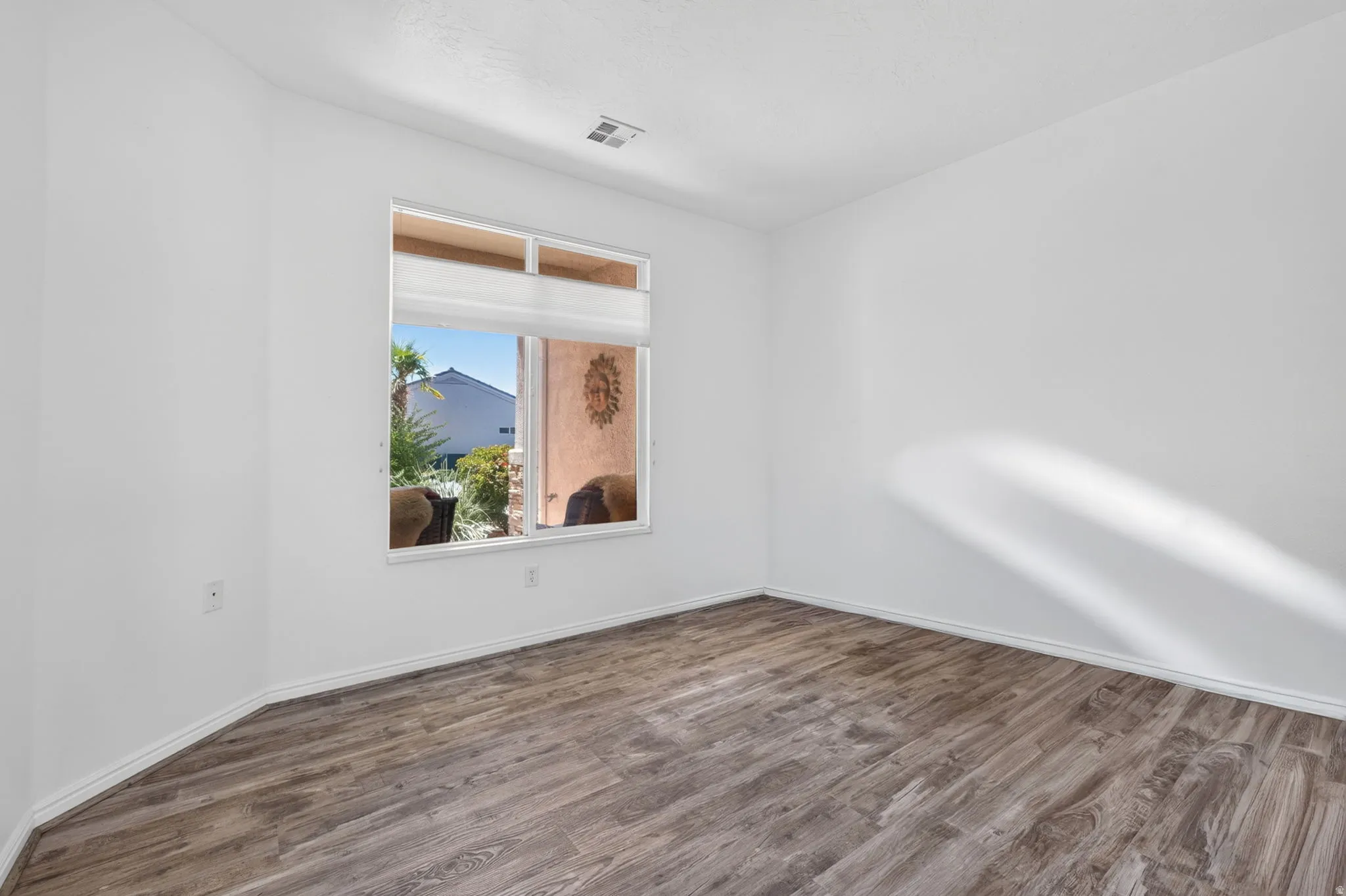 Room featuring wood-finish flooring, white baseboards, and a single window with a privacy blind