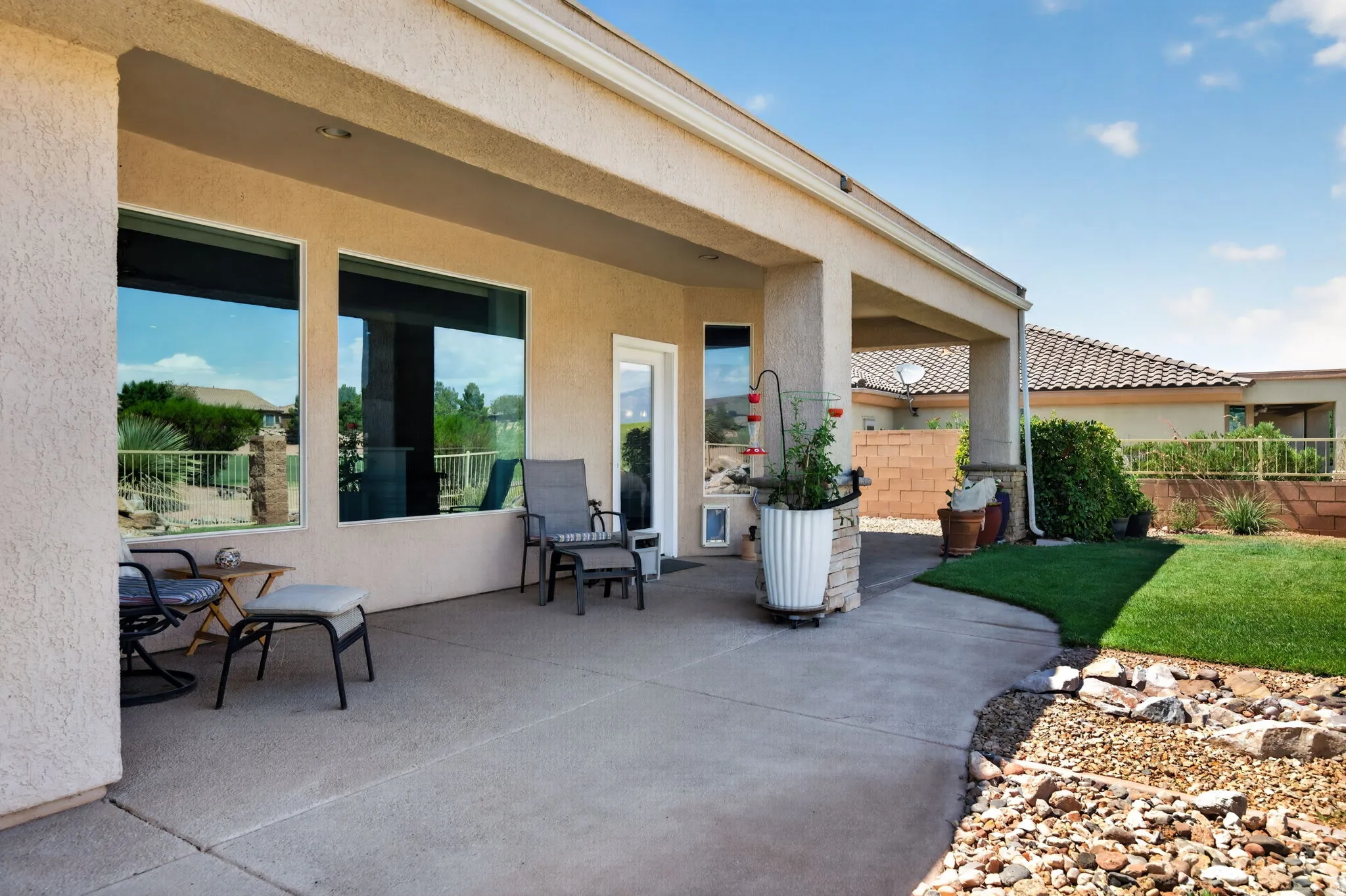 Covered patio with a concrete surface, featuring large windows and an exterior door