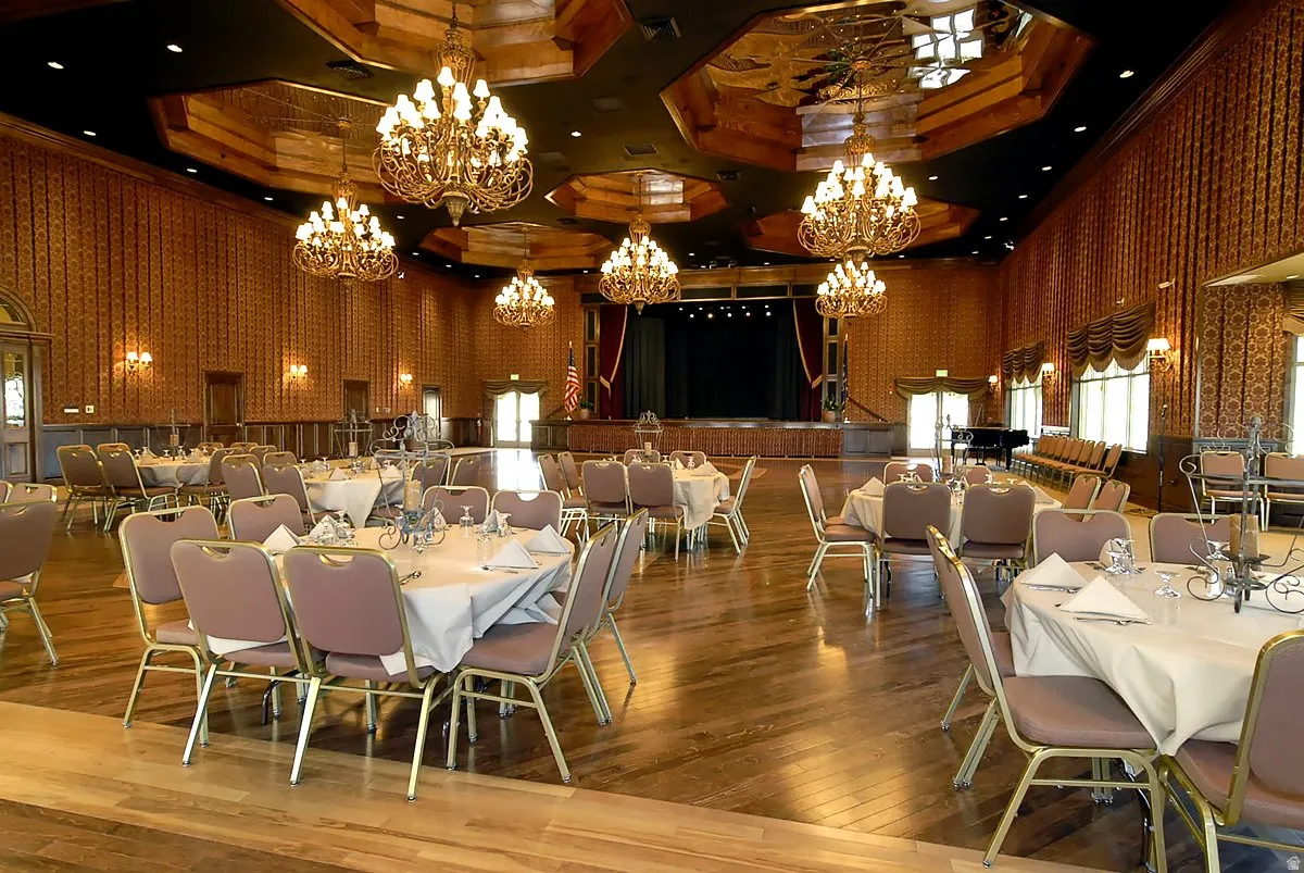 Spacious ballroom featuring a stage with curtains, multiple chandeliers, wood-finish flooring, and patterned wall coverings