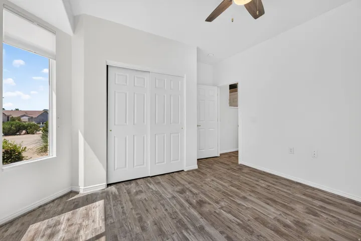 Room with wood-finish flooring, a ceiling fan with integrated lighting, and a window featuring a roller shade
