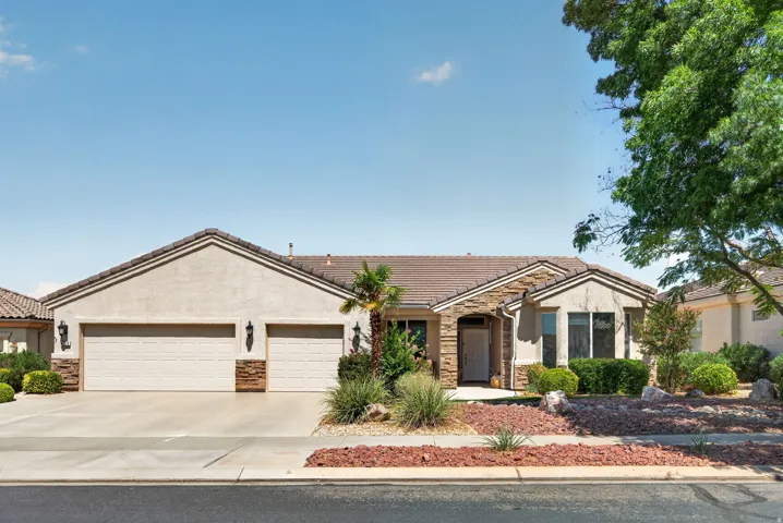 Stucco exterior residence featuring a tiled roof, stone accents, two-car garage, and desert-adapted landscaping