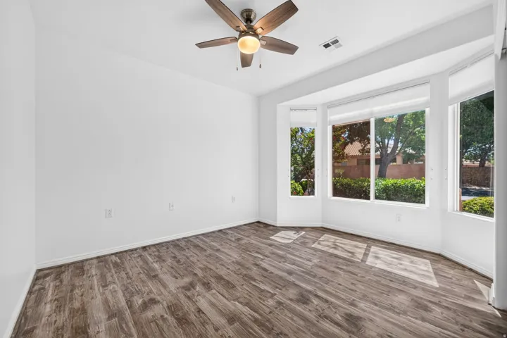 Spacious room featuring wood-finish flooring, a contemporary ceiling fan, and a multi-pane bay window with roller shades