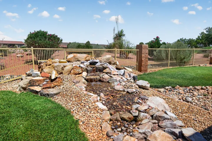 Outdoor water feature with natural rockery and flowing water, bordered by a manicured lawn and decorative gravel landscaping