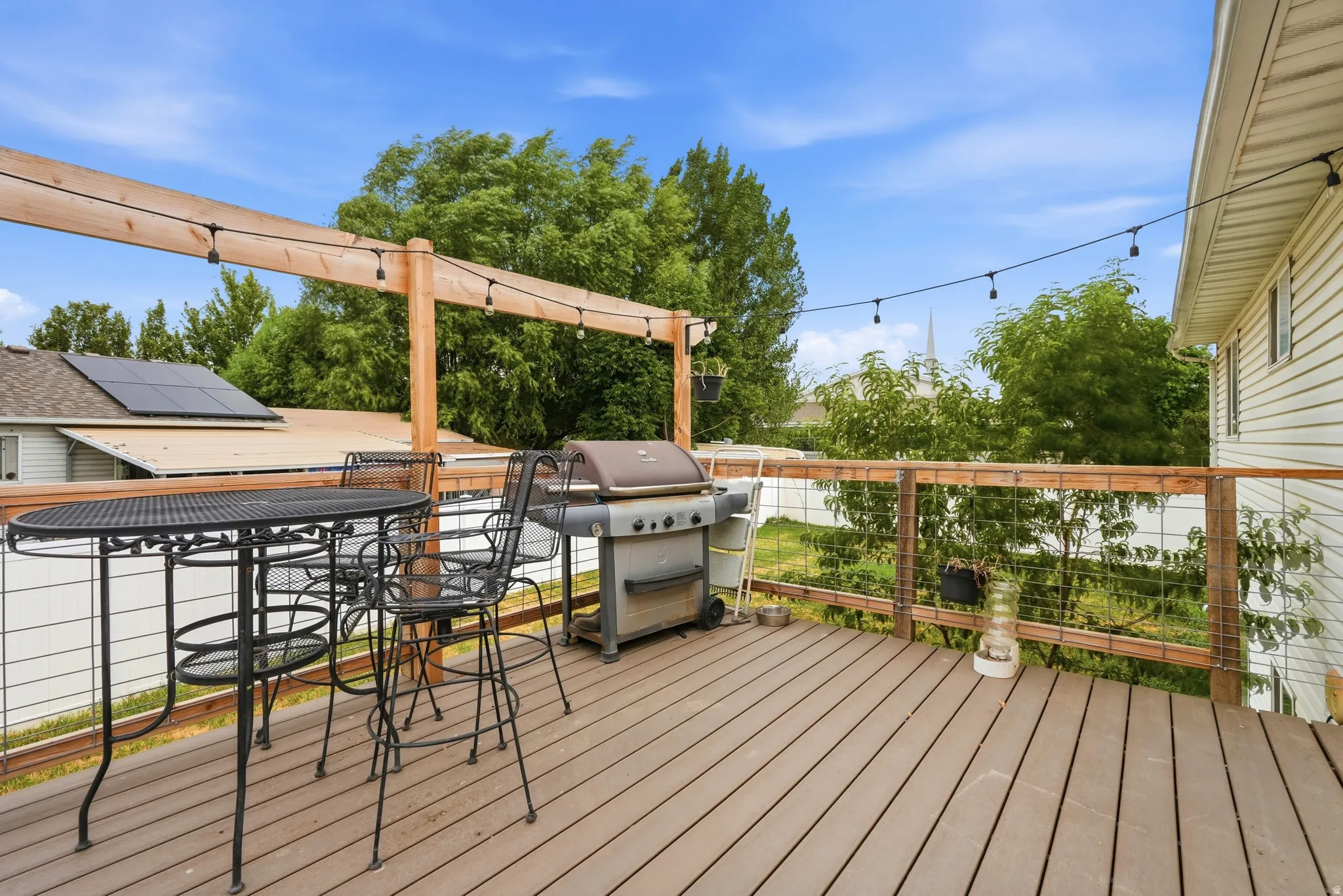 Spacious outdoor deck featuring composite wood-finish decking, wire railing, and overhead string lighting