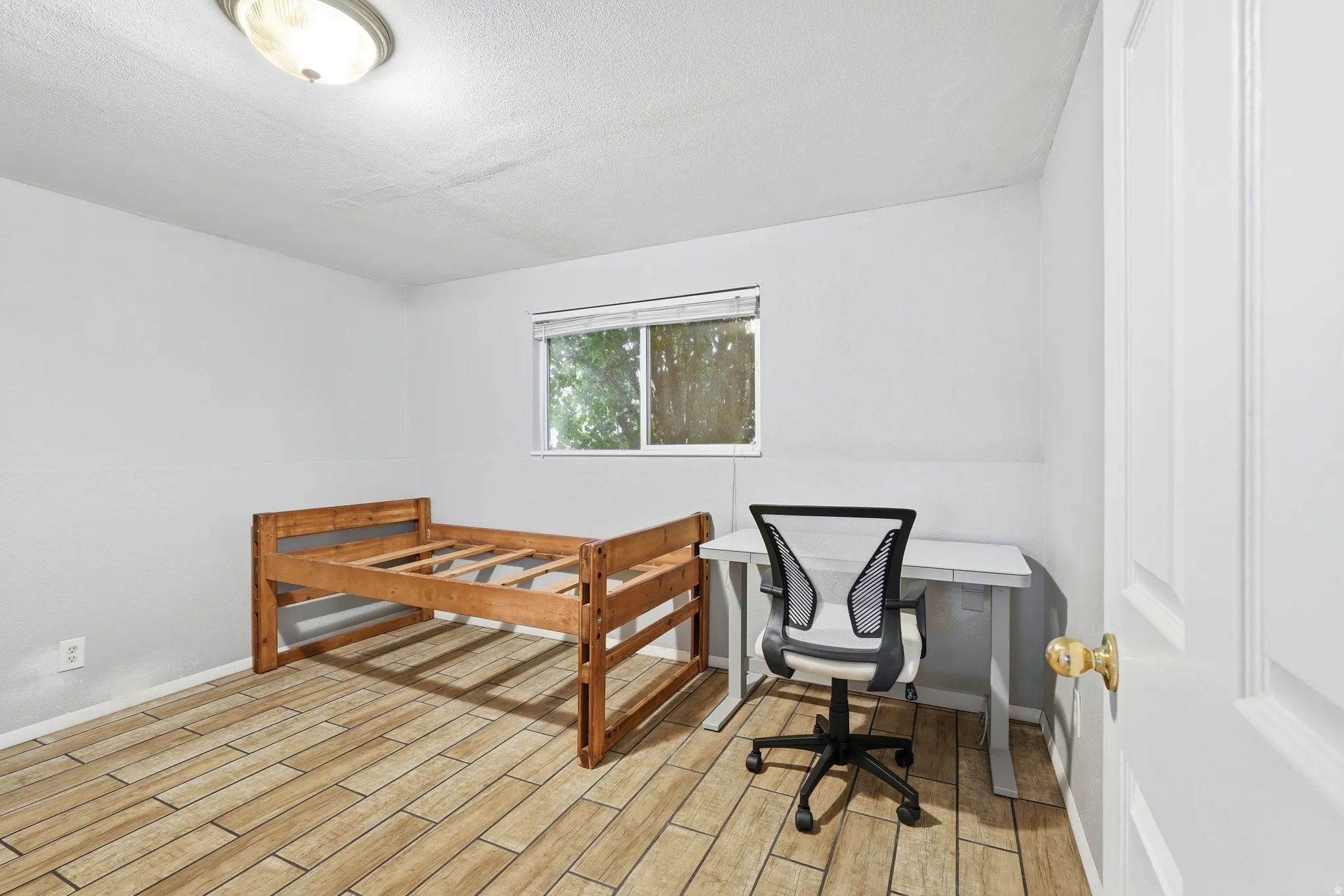 Room featuring wood-finish tile flooring, a window with horizontal blinds, and a white interior door with a brass knob