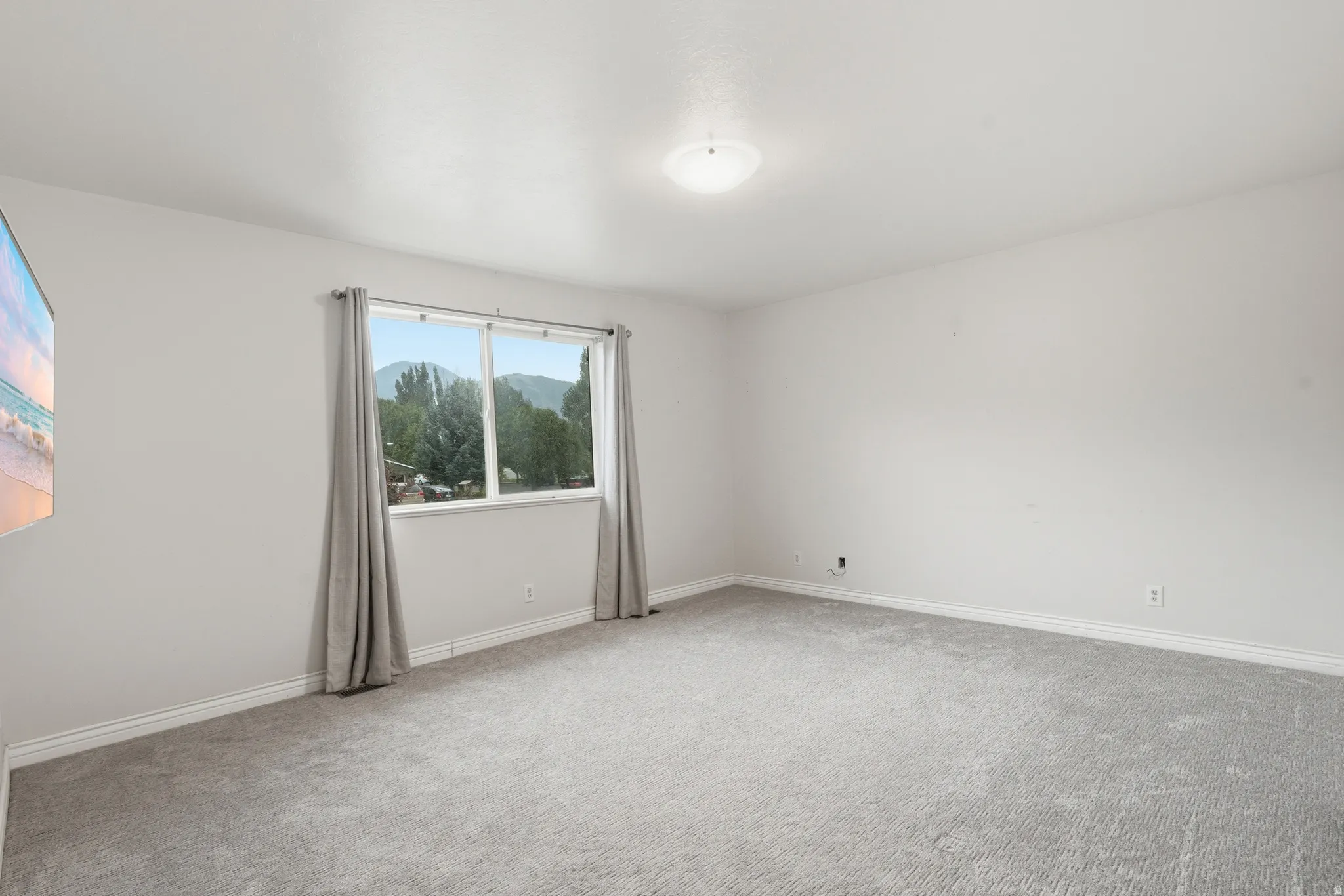Expansive room featuring light gray carpeting, crisp white walls, and a large window framing distant mountains and lush greenery