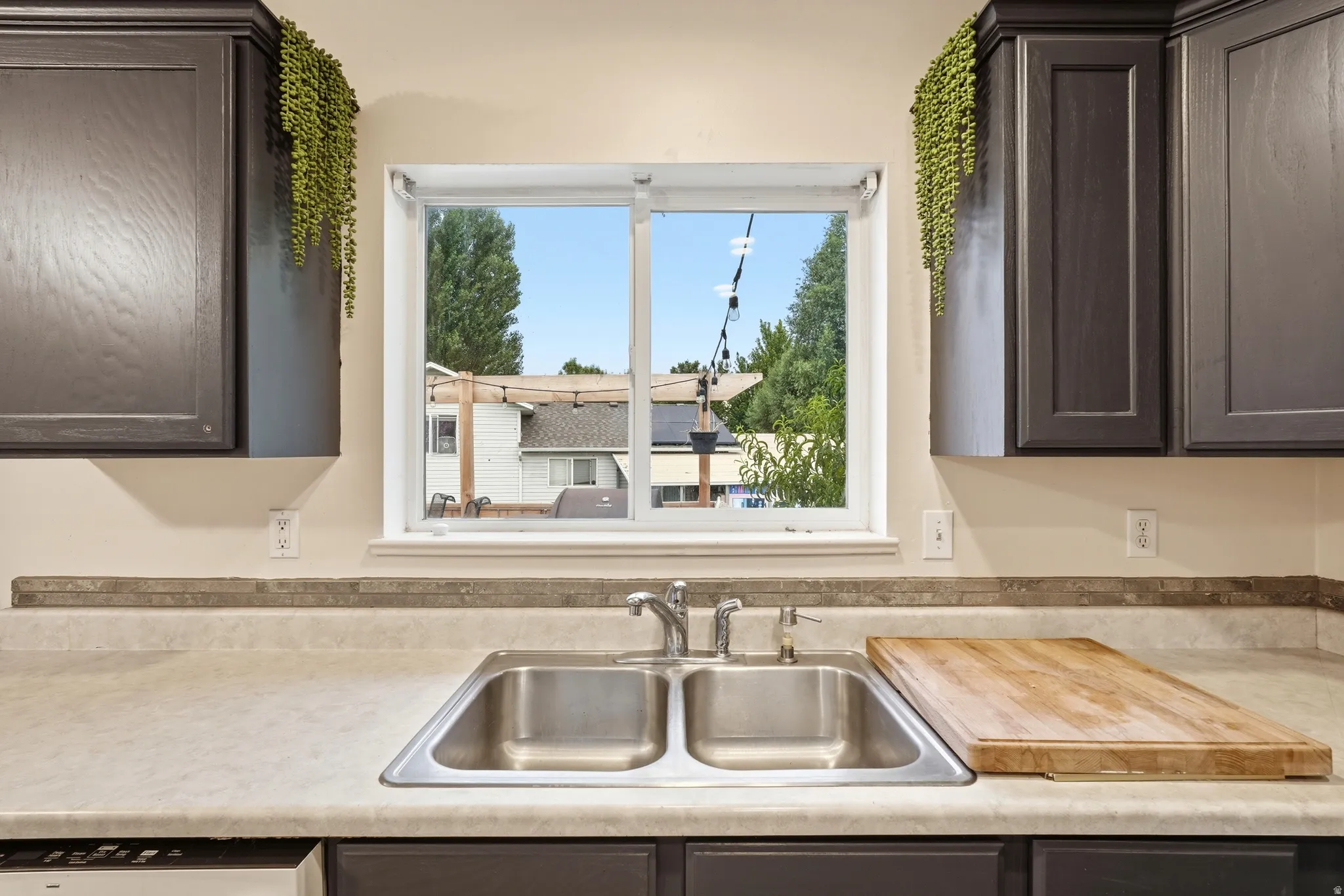 Kitchen features a double basin stainless steel sink with a chrome faucet, under-window placement, and light-toned countertops