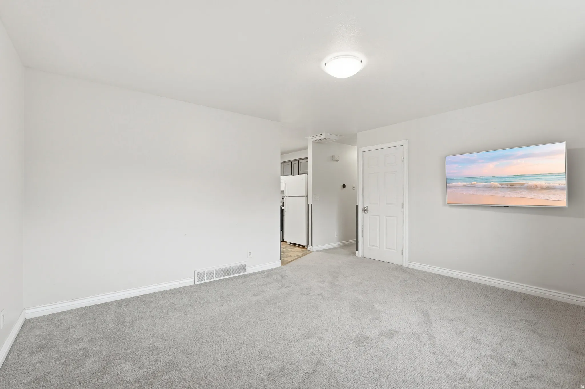Bright interior space featuring light gray carpeting, white painted walls, and white baseboards