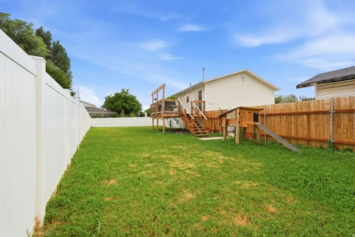Expansive backyard featuring a large grass area, a white vinyl privacy fence, and a wooden deck with stairs