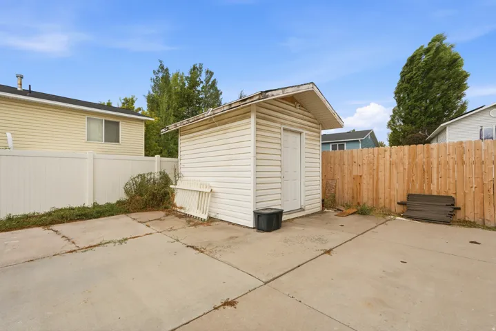 Concrete patio area featuring a storage shed with vinyl siding, a white privacy fence, and a natural wood fence
