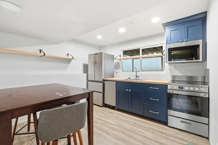 Kitchenette featuring blue shaker-style cabinetry with chrome hardware, wood-finish countertops, stainless steel appliances, and wood-finish flooring