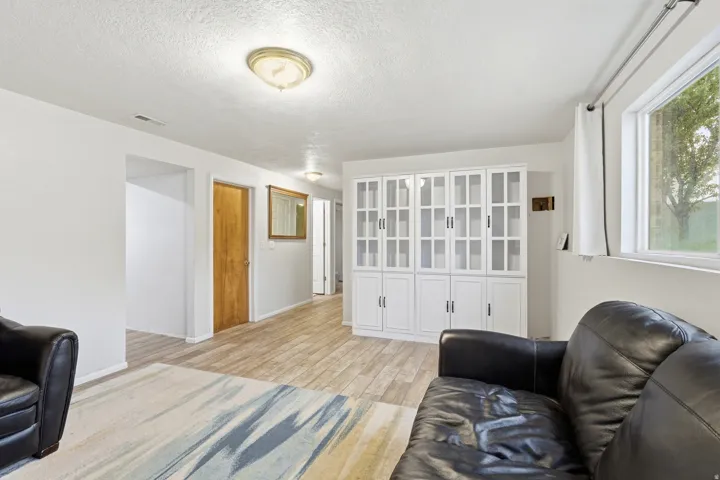 Built-in white cabinetry with glass-front doors, light wood-finish flooring, white walls, and a large window providing natural illumination