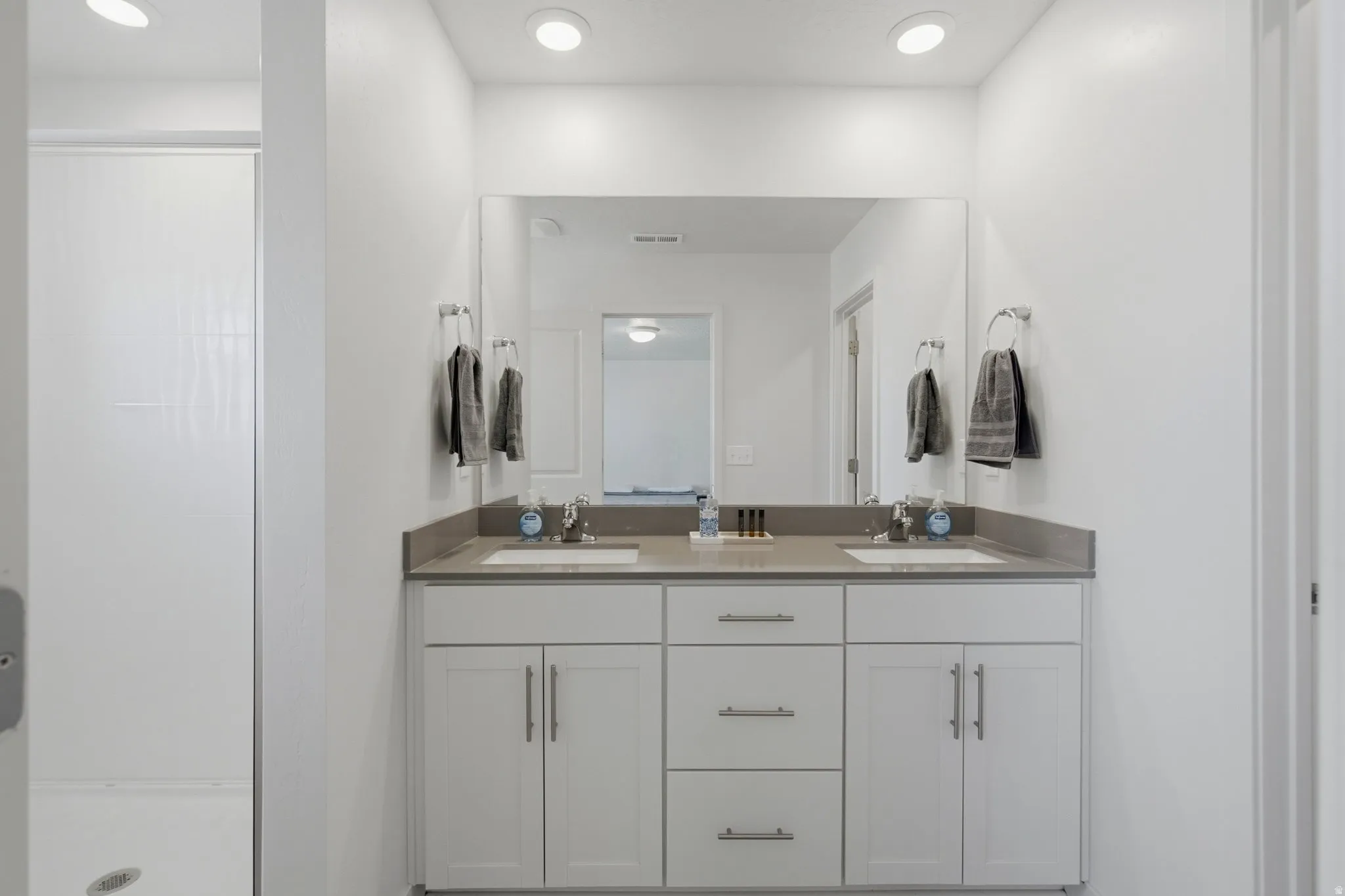 Bathroom featuring a double vanity with an integrated countertop, undermount sinks, and white shaker-style cabinetry with brushed nickel hardware