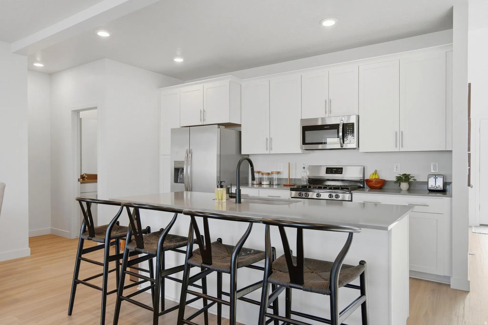 Modern kitchen featuring white cabinetry, stainless steel appliances, a large island with seating, recessed lighting, and wood-finish flooring