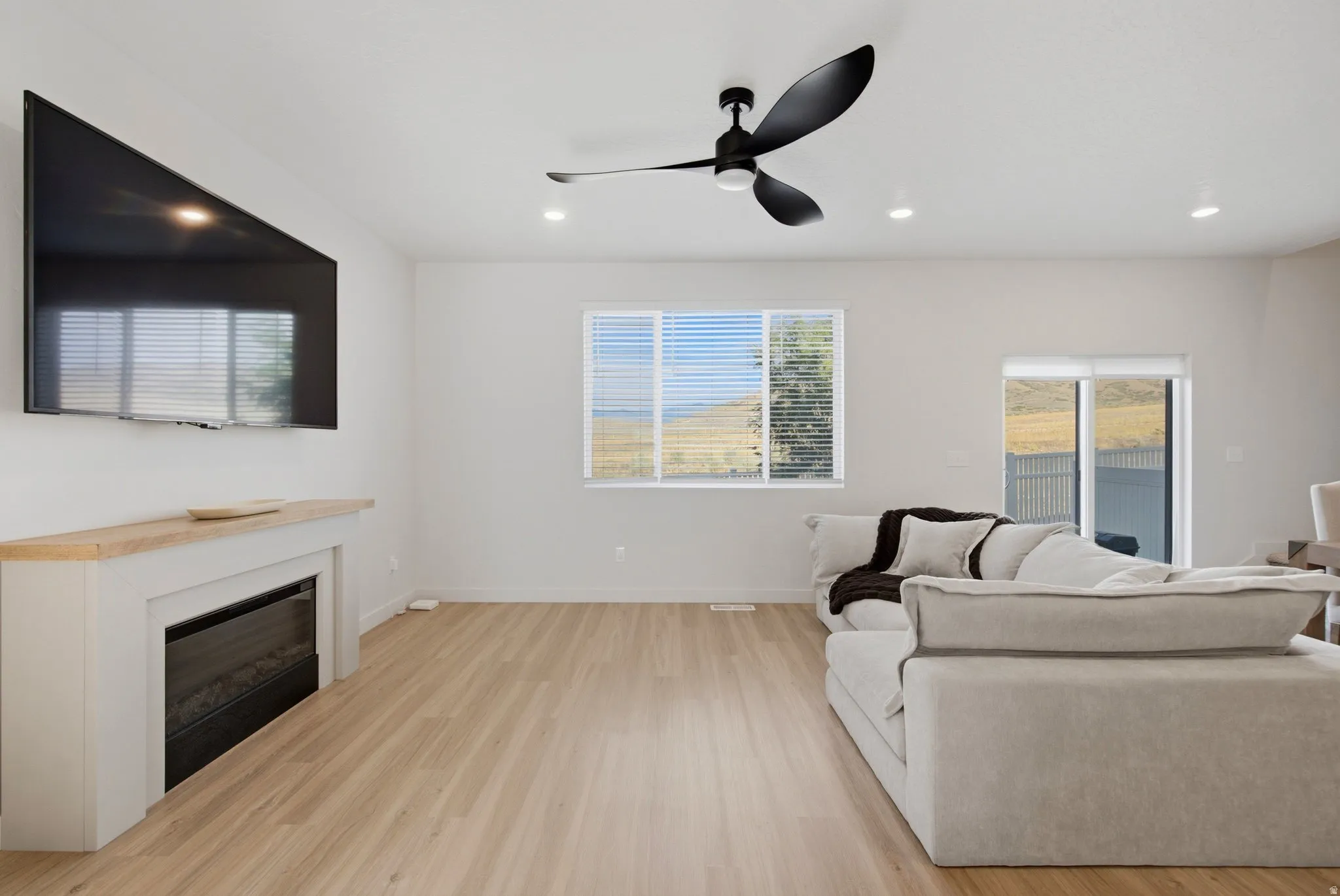 Bright living area featuring wood-finish flooring, a built-in fireplace with a wooden mantel, a modern ceiling fan, recessed lighting, and a sliding glass door