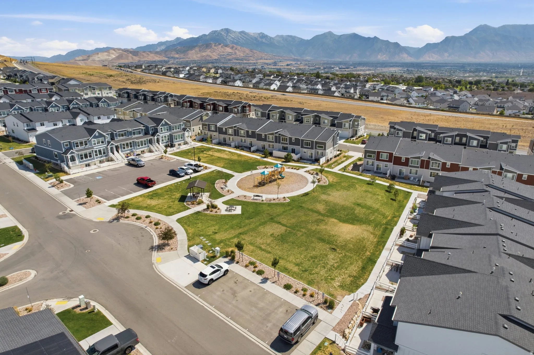 Expansive green space featuring a playground, walking paths, and mature landscaping, surrounded by multi-story residential properties with mountain scenery