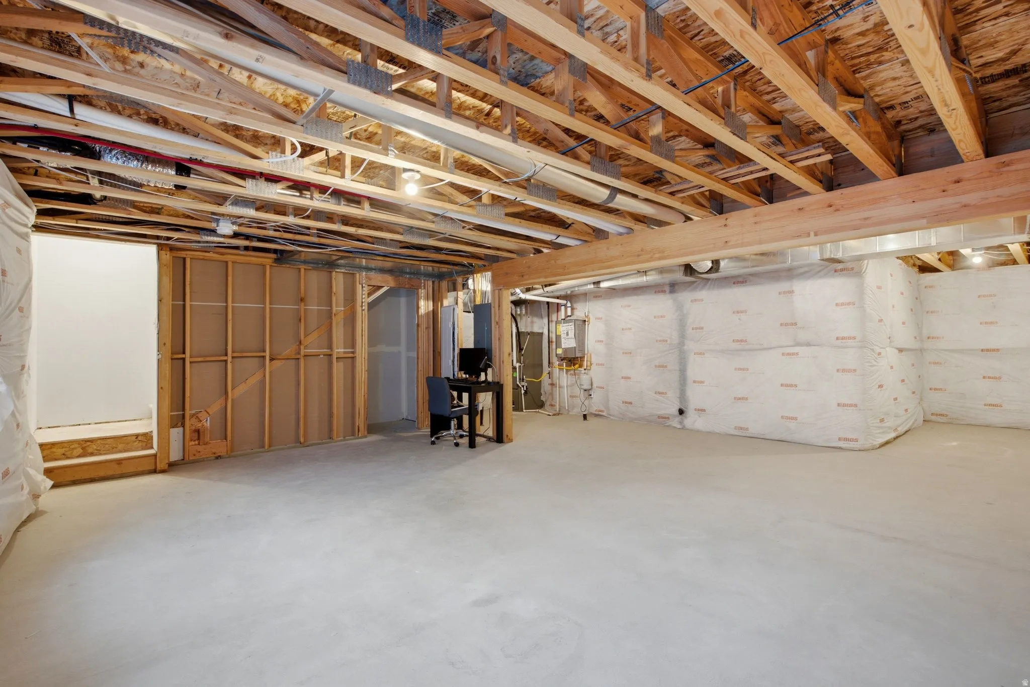 Spacious unfinished lower level featuring exposed wood joists, concrete flooring, insulated perimeter walls, and framed interior walls