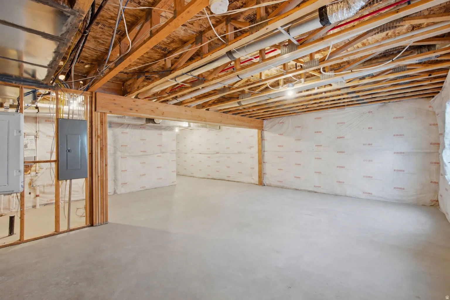 Spacious unfinished basement with exposed wood joists, concrete flooring, perimeter wall insulation, and visible electrical panels