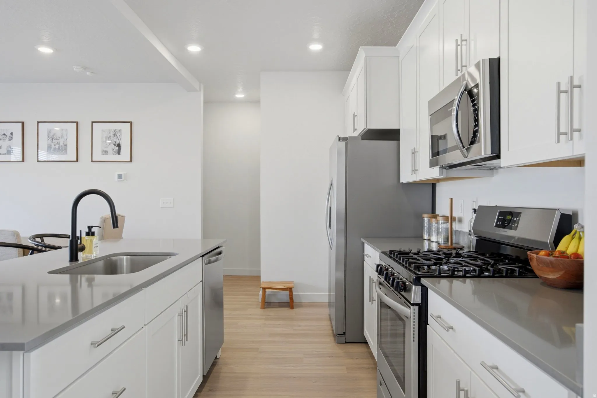 Bright kitchen featuring white cabinetry, stainless steel appliances, a center island with sink and matte black faucet, and wood-finish flooring