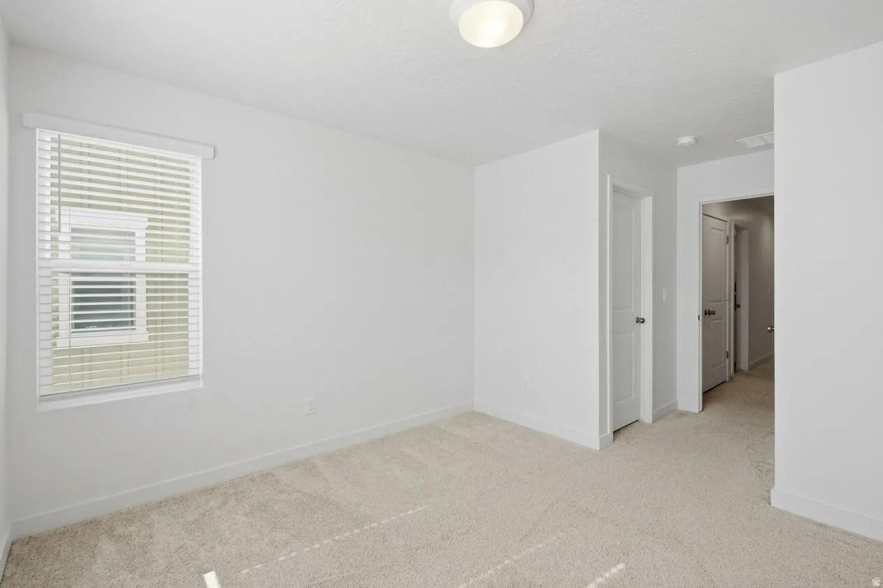 Neutral tone carpeting, white walls, flush mount ceiling light fixture, white window blinds, and white interior doors with round knob hardware