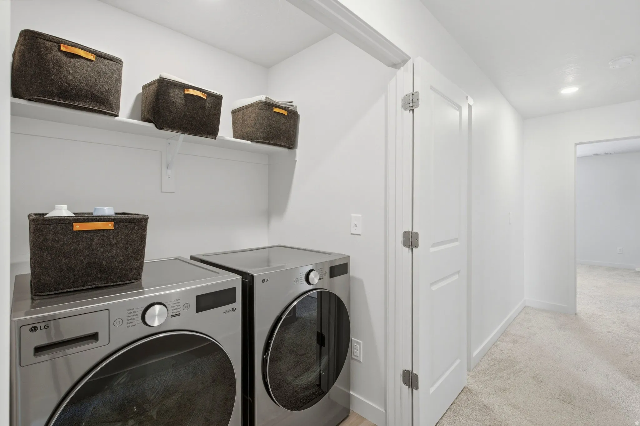 Dedicated laundry area featuring a built-in shelf, white walls, and light-toned carpeting extending through the hallway