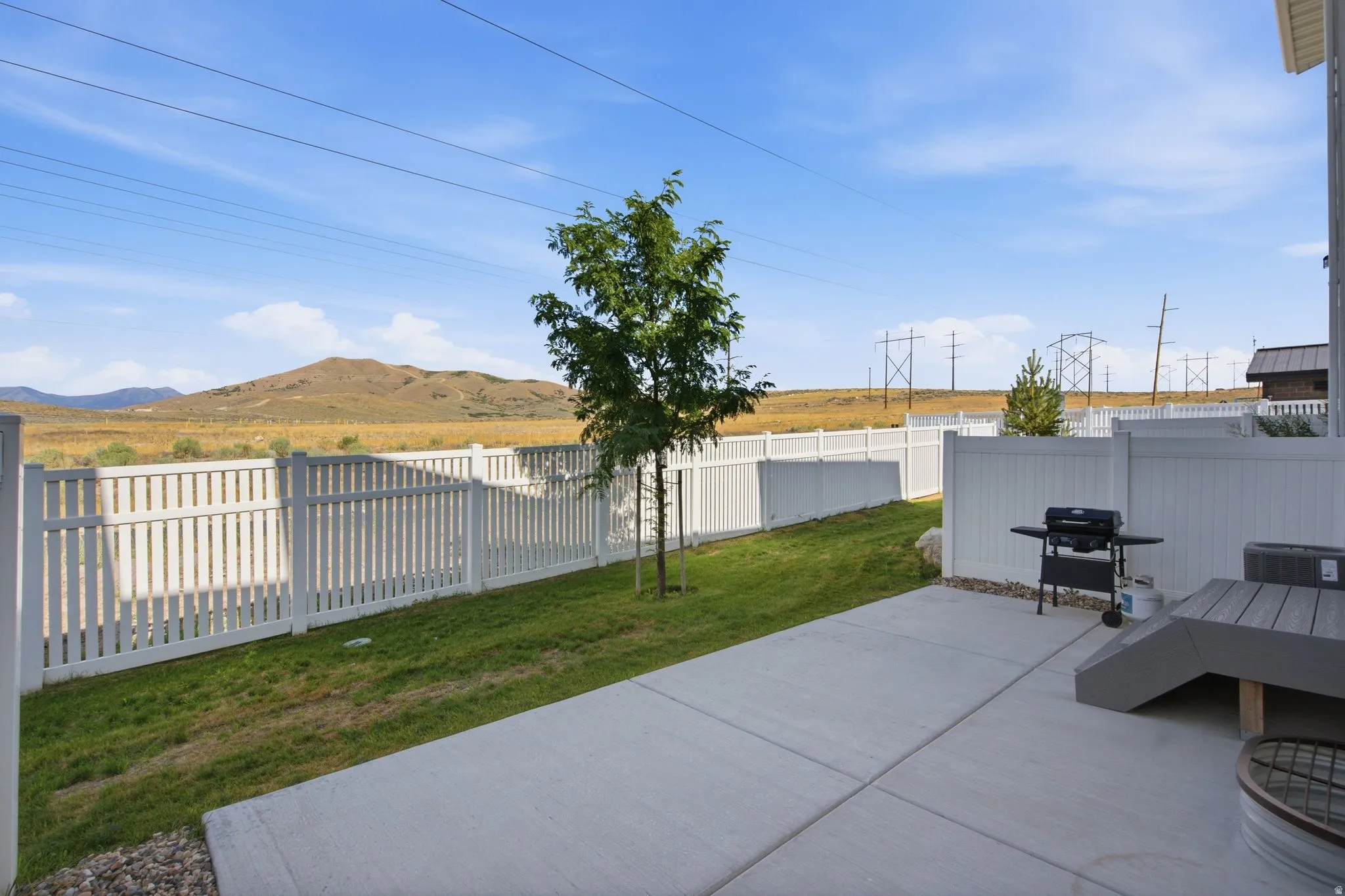 Concrete patio with a composite deck extension, white picket fencing, and a grassy yard area