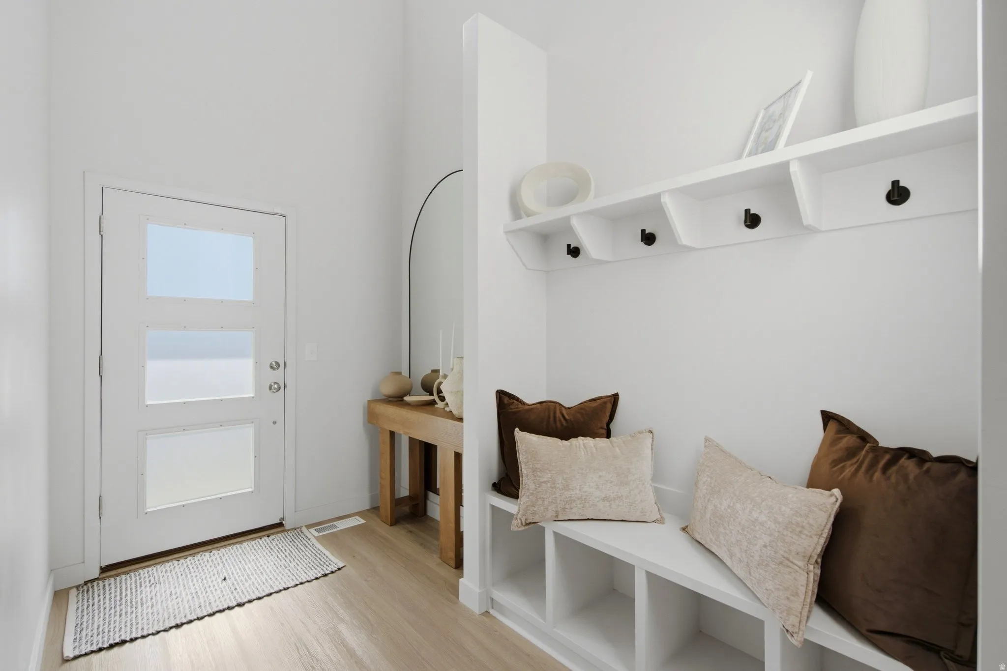 Entryway featuring a white door with three frosted glass panels, wood-finish flooring, and a built-in bench with integrated cubby storage