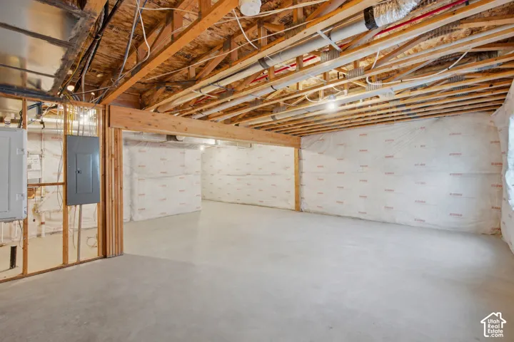 Spacious unfinished basement with exposed wood joists, concrete flooring, perimeter wall insulation, and visible electrical panels