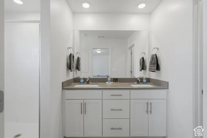 Bathroom featuring a double vanity with an integrated countertop, undermount sinks, and white shaker-style cabinetry with brushed nickel hardware