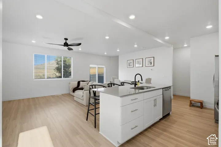 Open-concept living space featuring a central kitchen island with a single-basin sink and stainless steel faucet, wood-finish flooring, recessed lighting, and large windows