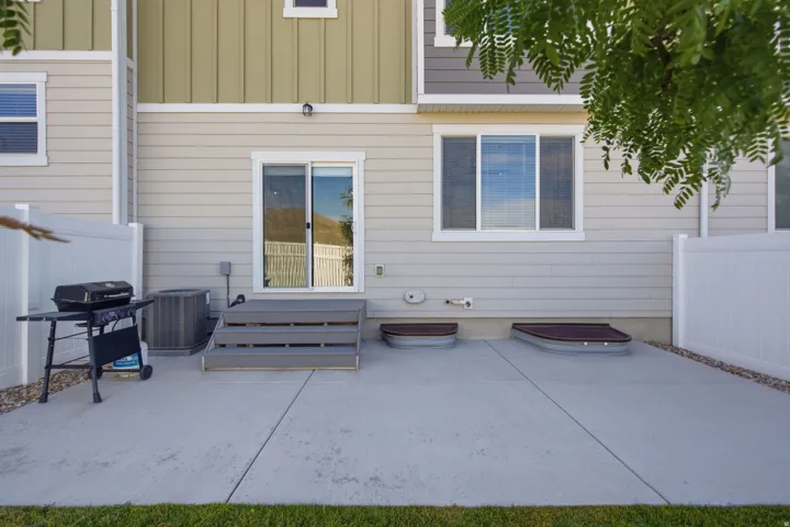 Concrete patio with a sliding glass door entry, grey composite steps, and two basement window wells