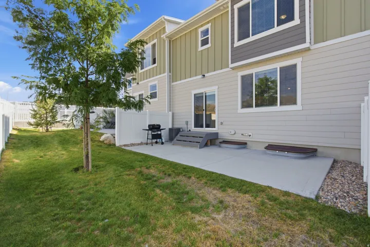 Rear exterior featuring a concrete patio, sliding glass door access, and a fenced yard with mature trees