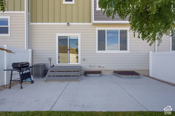Concrete patio with a sliding glass door entry, grey composite steps, and two basement window wells